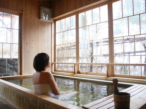 a girl sitting in a bath tub in a room with windows at Rankeisou in Sanjo