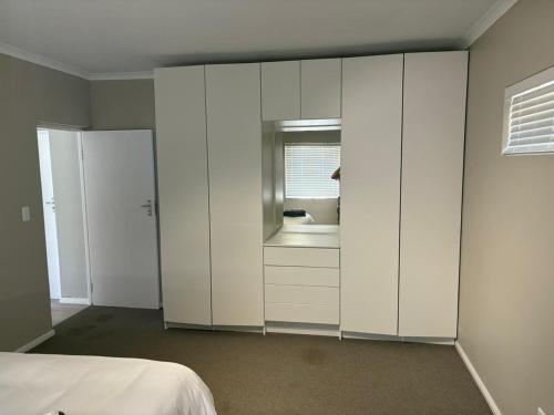 a white bedroom with white cabinets and a window at Jongensfontein Beachside Villa in Jongensfontein