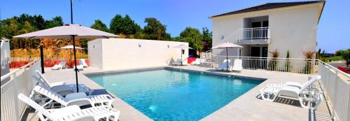 a swimming pool with white chairs and an umbrella at Bungalow on the sea - Moriani beach in Santa-Lucia-di-Moriani