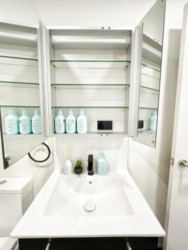a white bathroom with a sink and a mirror at Central Location Cozy Studio with Pool Gym & Sauna Nearby Skytower in Auckland