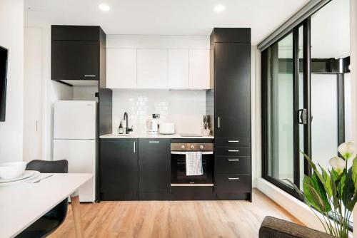 a kitchen with black cabinets and a white refrigerator at Cozy Aircon Studio Nearby Skytower - Pool Sauna Gym in Auckland