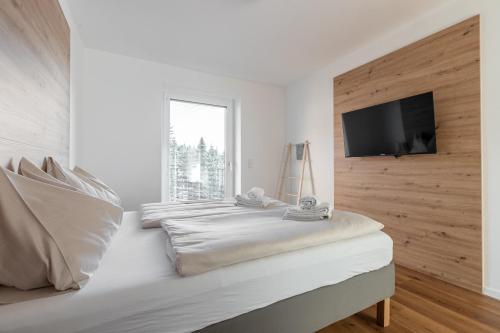 a white bedroom with a bed with a flat screen tv at Arton Lachtal - Apartments Steiermark in Lachtal