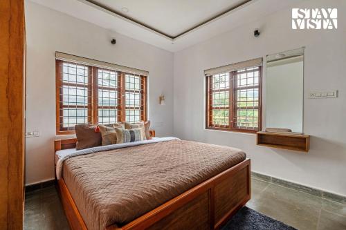 a bedroom with a bed and two windows at StayVista at Misty Village - BBQ, Bonfire & Meals in Pooppara