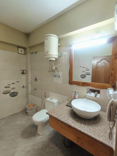 a bathroom with a sink and a toilet and a mirror at Regenta Inn by Riverside Manali in Manāli