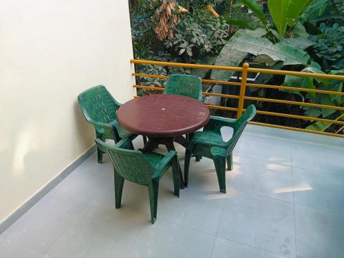 a wooden table and four green chairs on a balcony at Swarang hoomstye in Nandgaon
