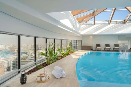 a large swimming pool in a building with windows at NH Collection Plaza Santiago in Santiago