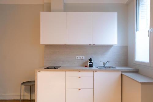 une cuisine avec des armoires blanches et un évier dans l'établissement Majestic Suites - Paris 11, à Paris
