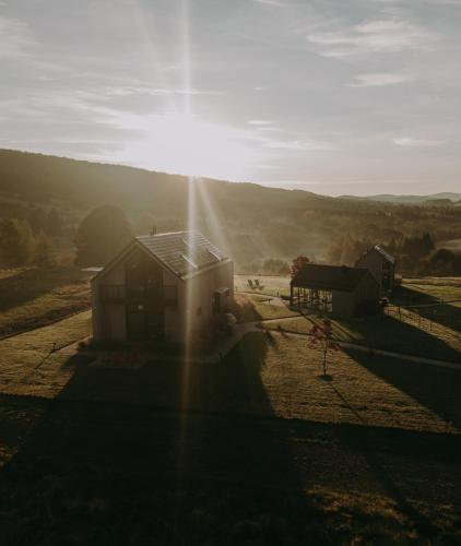 a house in a field with the sun shining behind it at Bieszczadzka Stodoła in Ustrzyki Dolne