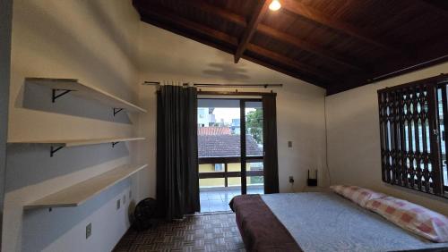 ein Schlafzimmer mit einem Bett und einem großen Fenster in der Unterkunft Casarão até 8 pessoas 400m mar Bombinhas in Bombinhas