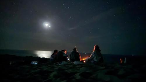 a group of people sitting around a fire on the beach at night at Moroccan Boho Surf House in Agadir