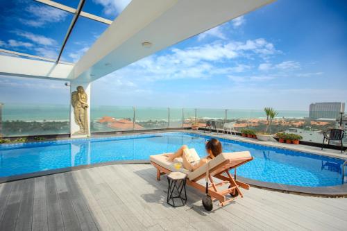 a woman sitting in a chair next to a swimming pool at Sea Phoenix Hotel Da Nang in Danang