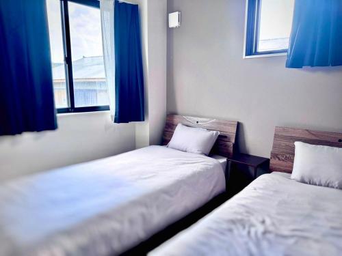two beds in a small room with blue curtains at AZホテル inn 奄美佐仁 Ocean View in Sani