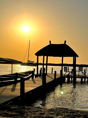 un muelle con la puesta de sol sobre el agua con un barco en Mbin Maak du Saloum, en Mar Lodj