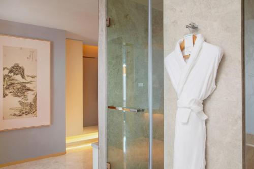 a white robe hanging on a glass shower door at Le Meridien Hangzhou, Binjiang in Hangzhou