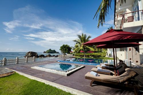 a pool with chairs and an umbrella next to the ocean at Garton's Cape in Ahangama