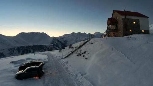 two cars parked in the snow next to a building at Family Hotel Parnas 2250 in Gudauri