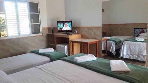 a room with three beds and a desk with a television at Hotel Fazenda e Pesqueiro Pousada da Serra in Goianésia