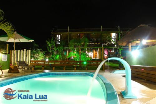 a swimming pool in front of a hotel at night at Pousada Cabanas Kaia Lua in Praia do Rosa