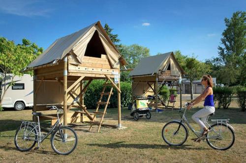 une femme faisant du vélo devant une maison de jeu dans l'établissement Camping Onlycamp Le Petit Port, à Châtel-Censoir