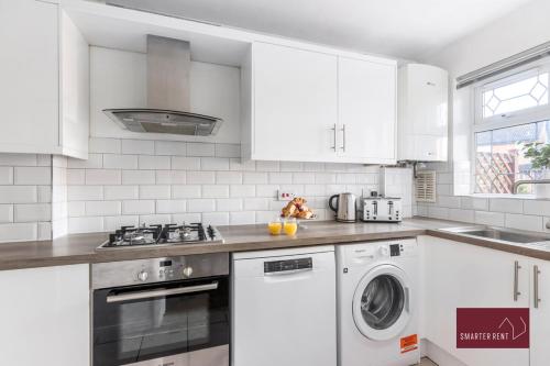 a kitchen with white cabinets and a washer and dryer at Guildford - Two Bed House in Guildford