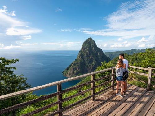 a man and a woman standing on a wooden walkway overlooking the ocean at Sugar Beach, A Viceroy Resort in Soufrière