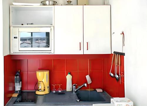 - une cuisine avec des murs rouges et des armoires blanches dans l'établissement Appartement charmant à Saint-Cyprien avec vue sur la mer - 24m², à Saint-Cyprien