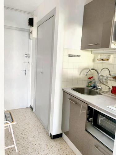 - une cuisine blanche avec un évier et une porte dans l'établissement Studio charmant & lumineux à La Grande-Motte - 22 m² + Balcon, à La Grande Motte