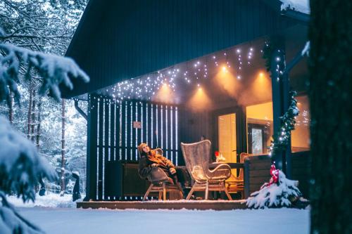 a woman sitting on the porch of a house with christmas lights at Cocodeno-'Virš Ąžuolų' - Forest SPA - FREE jacuzzi in Paplatelė