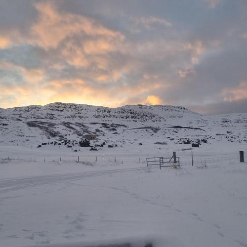 a snow covered field with a fence and a mountain at Hvammur 10 with private hot tub in Kaldrananes