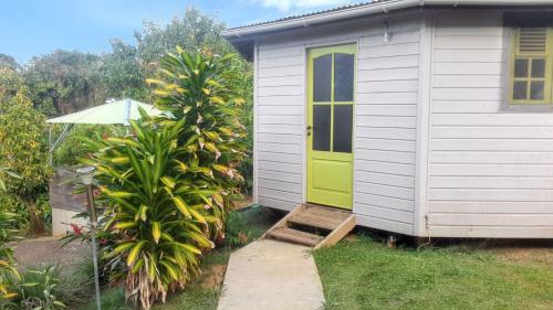 a small house with a green door and a palm tree at Bungalow charmant au Robert avec piscine partagée et jardin in Le Robert