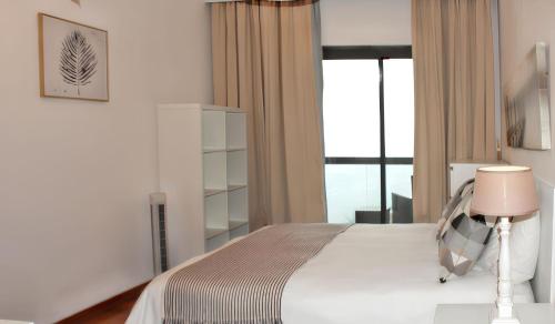 Un dormitorio con una cama con una lámpara y una ventana. en Spacious house with sea view in Caniço + private pool, en Caniço