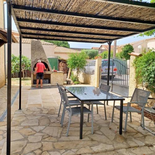 a man standing on a patio with a table and chairs at Appartement charmant à Vias + jardin in Vias