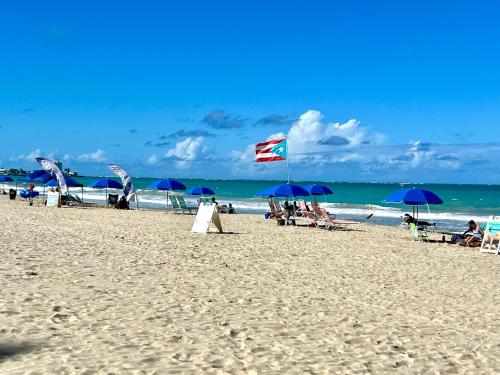 a beach with blue umbrellas and people on the sand at Private Apartment at Maré St Clair Hotel in San Juan