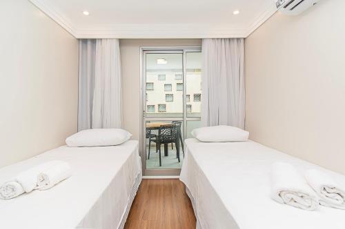 two beds in a room with a table and a window at BSB STAY Torre Flats Particulares - Mercure Líder in Brasilia