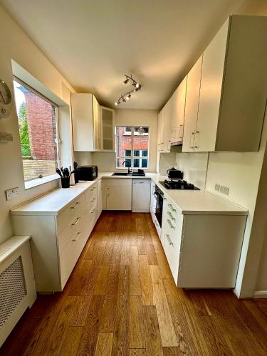 a kitchen with white cabinets and a wooden floor at Quiet residential area modern and cozy two bed apartment in Hampstead in London