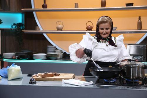 a woman in a kitchen preparing food in a skillet at Pensiunea Inima Maramureșului in Breb