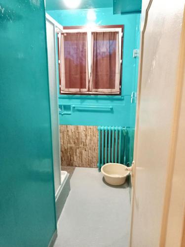 La salle de bains bleue est pourvue de toilettes et d'une fenêtre. dans l'établissement Maison accueillante à Montluçon avec jardin privatif, à Montluçon