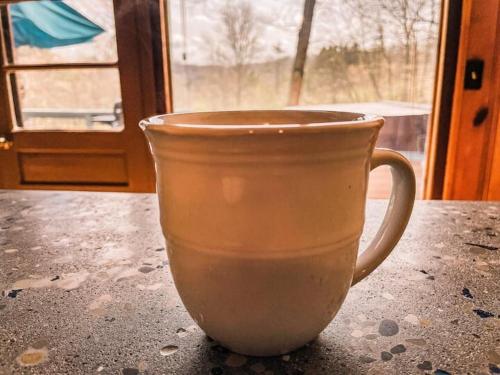 a coffee cup sitting on a table in front of a window at Whispering Waters, Hocking Hills, Hot Tub, Pond in Rockbridge
