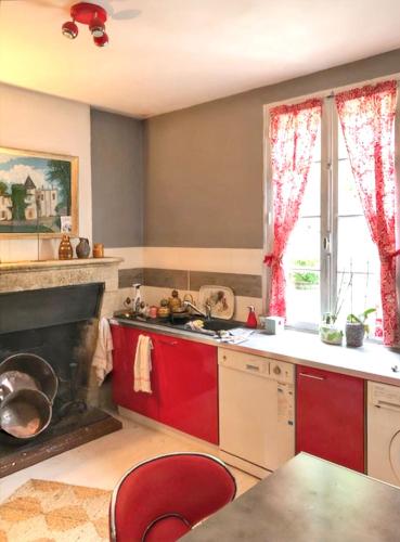 une cuisine avec des placards rouges et une cheminée dans l'établissement Maison charmante au cœur de Sainte-Croix-du-Mont avec jardin, à Sainte-Croix-du-Mont