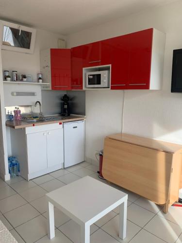 - une petite cuisine avec des placards rouges et une table blanche dans l'établissement Studio Carnon plage face au port, à Mauguio