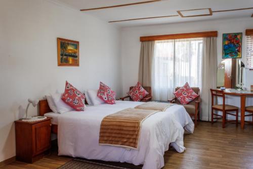 a bedroom with a bed with red pillows and a table at Haus Garnison B&B in Swakopmund