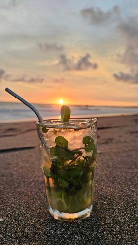 a drink on the beach with a sunset in the background at Mano a Mano Eco Hostal in Las Peñitas