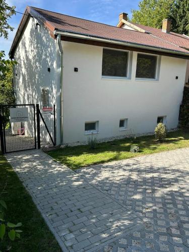 a white house with a gate and a brick driveway at Sun&Fun Vendégház in Balatonakarattya