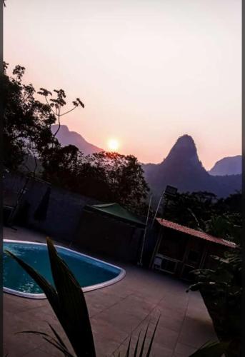 a sunset over a swimming pool with mountains in the background at Recanto da Cachoeira RJ in Magé