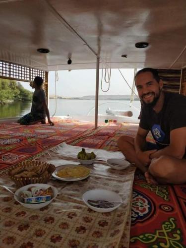 a man sitting on a boat with food on the floor at Mama Africa Felucca in Aswan