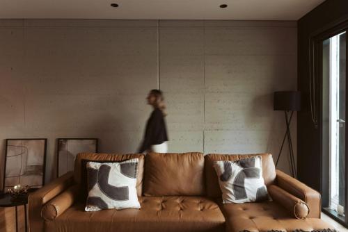 a person standing in a living room with a brown couch at Romantic Lakefront Luxury - Spa Bath, Fireplace, King Bed in Daylesford