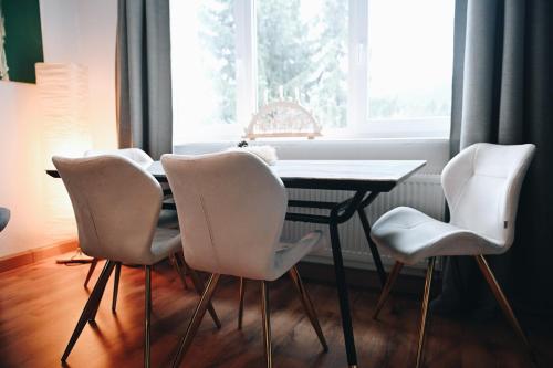 a dining room table with four white chairs and a window at Oberwiesenthal Apartments in Kurort Oberwiesenthal