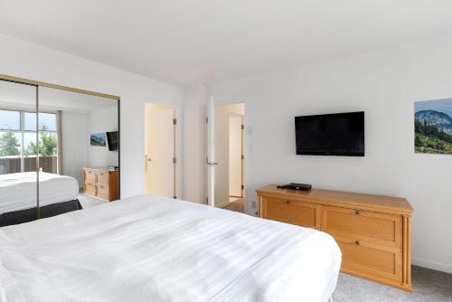 a white bedroom with a bed and a tv on a wall at The Woodrun Lodge by Whiski Jack in Whistler