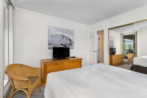 a white bedroom with a bed and a tv at The Woodrun Lodge by Whiski Jack in Whistler