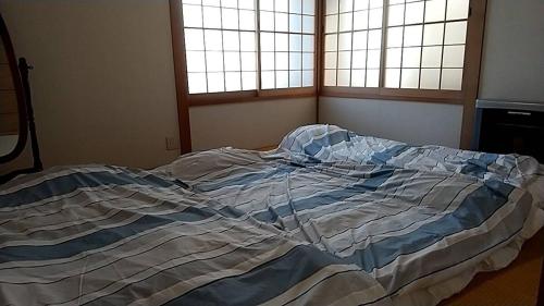 an unmade bed in a bedroom with two windows at 10-minute walk from Hakodate station, entire house, up to 10 people in Hakodate